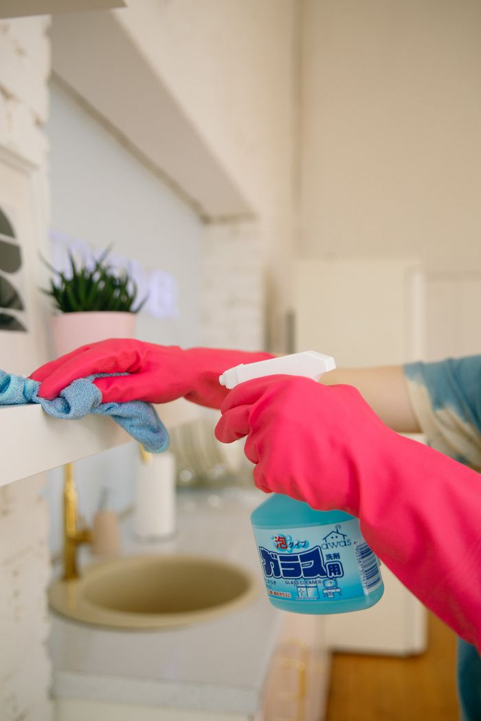 services-02 Person using spray bottle and cloth for cleaning a kitchen shelf, ensuring hygiene and cleanliness.